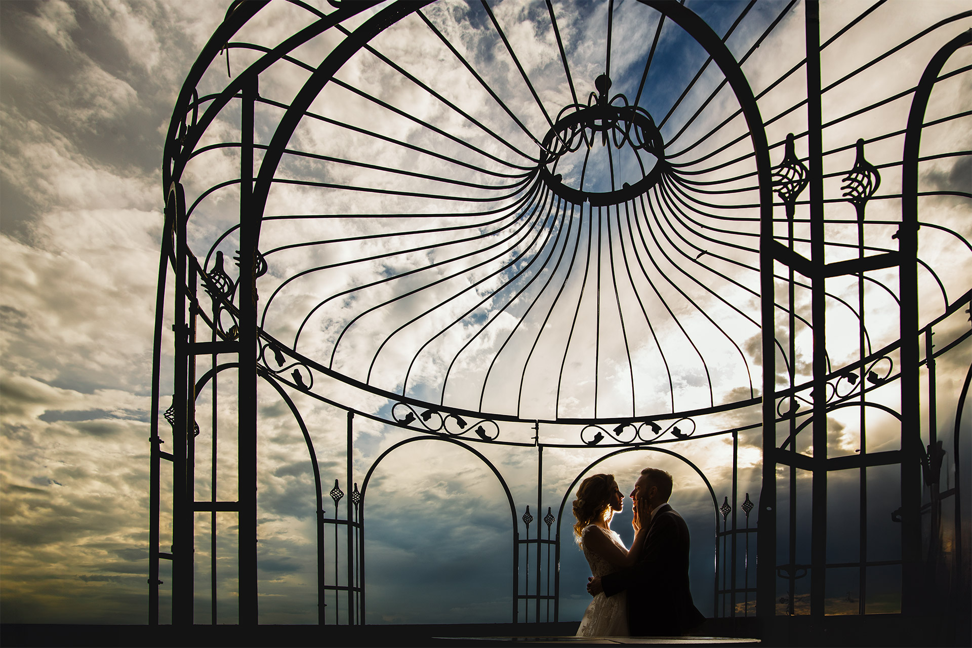 Matrimonio al Castello di Cortanze. Sessione di Coppia. Sposi sotto un gazebo in ferro battuto con cielo drammatico e flash esterno dietro gli sposi.