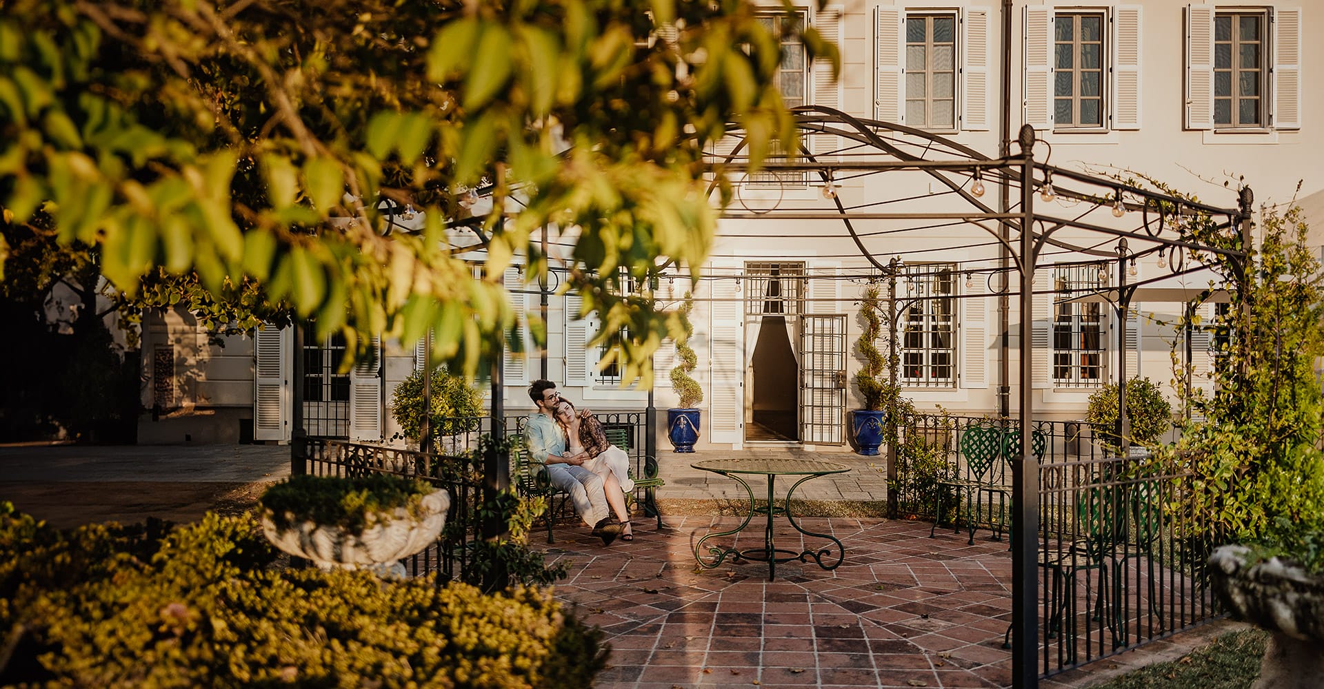 Fotografo matrimonio Rivalba. Villa Ala. Prewedding di Giorgia e marco. La coppia è seduta abbracciata su di una panchina di ferro sotto un romantico gazebo in ferro battuto. Golden hour